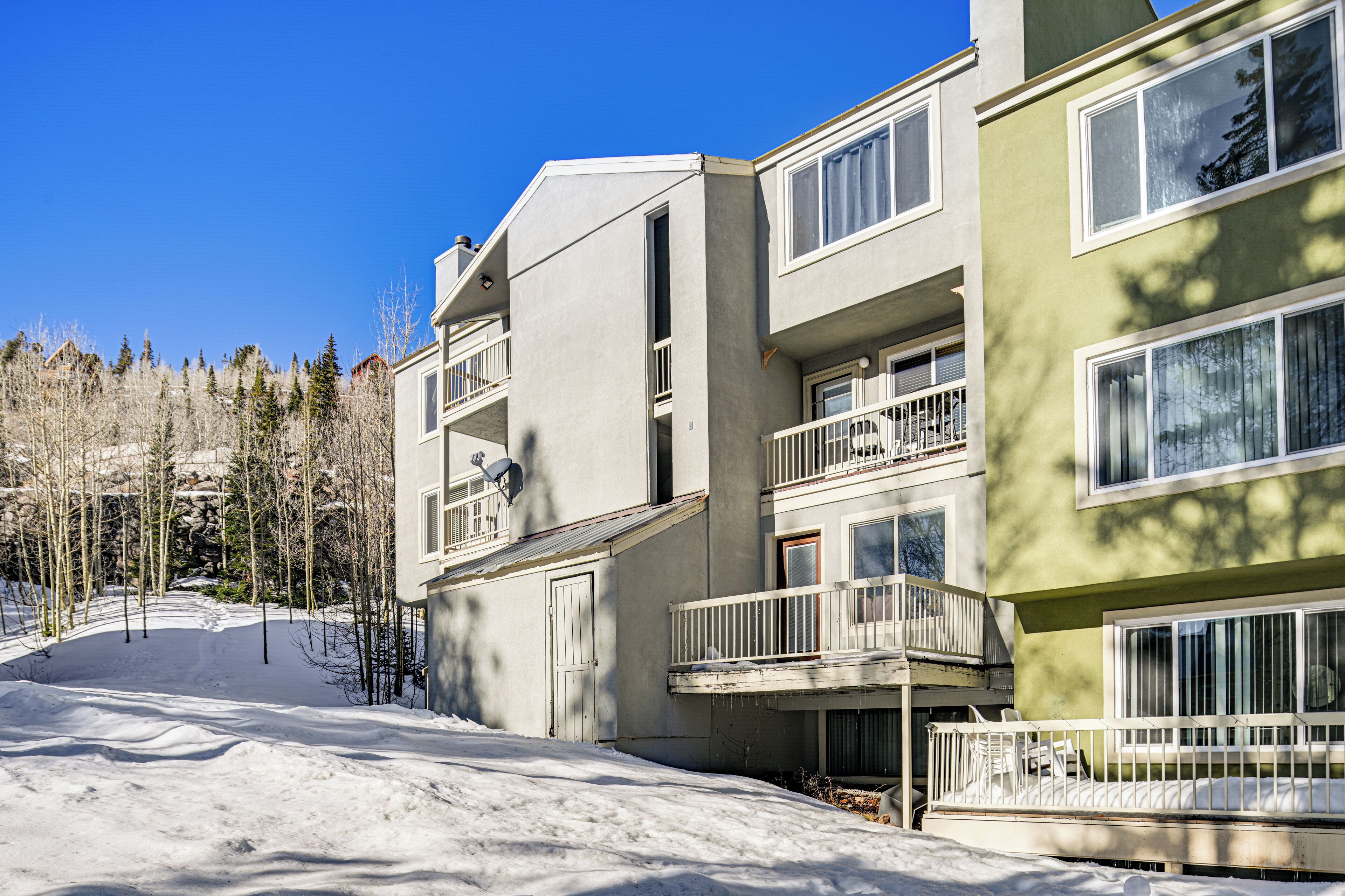 A multi-story building with balconies and large windows, surrounded by snow and trees.