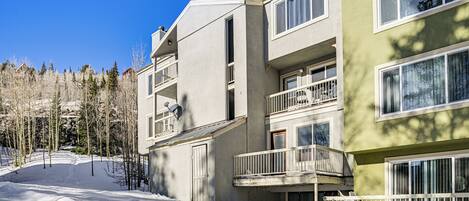 A multi-story building with balconies and large windows, surrounded by snow and trees.