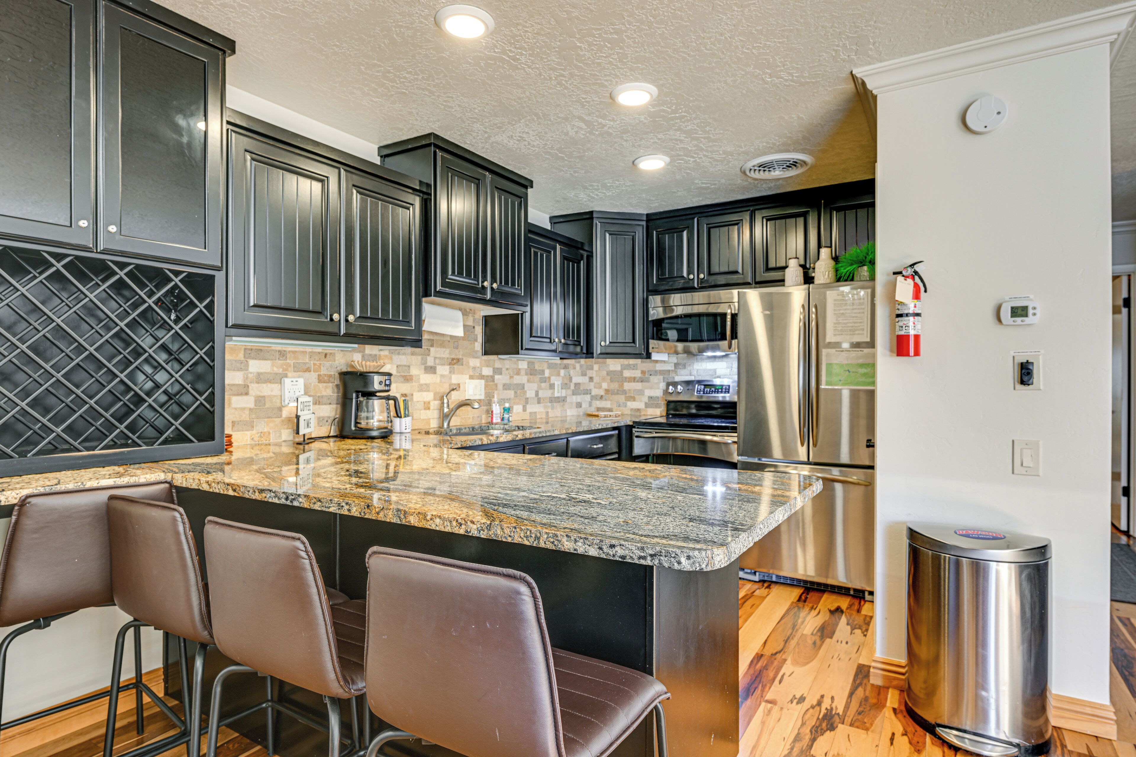 A modern kitchen with dark cabinets, granite countertops, stainless steel appliances, and a bar area with stools.