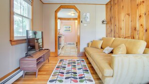 A living room with a wooden floor, a sofa, a TV, and a rug. - Walk to Grays Beach Park: Kingston Seaside Escape (Kingston)