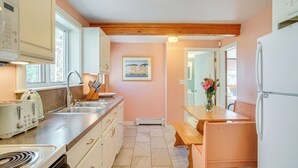A kitchen with a wooden beam ceiling, a sink, a stove, and a dining area with a bench. - Walk to Grays Beach Park: Kingston Seaside Escape (Kingston)