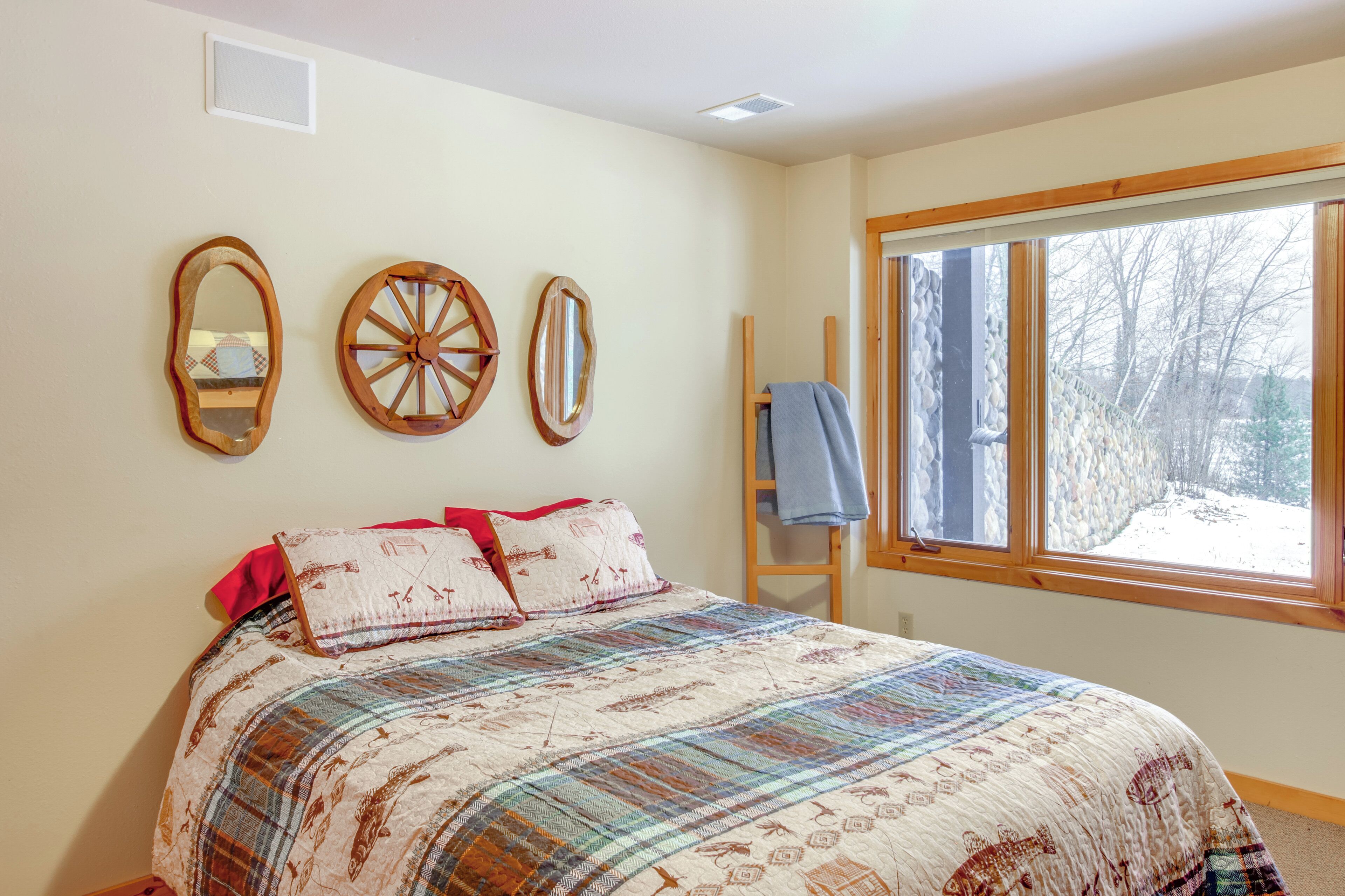 A bedroom with a large bed, three wall mirrors, a window with a view of trees, and a wooden ladder leaning against the wall.