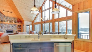 Une cuisine spacieuse dotée d’un grand îlot central, d’un plafond en bois et de grandes fenêtres offrant une vue sur l’extérieur.