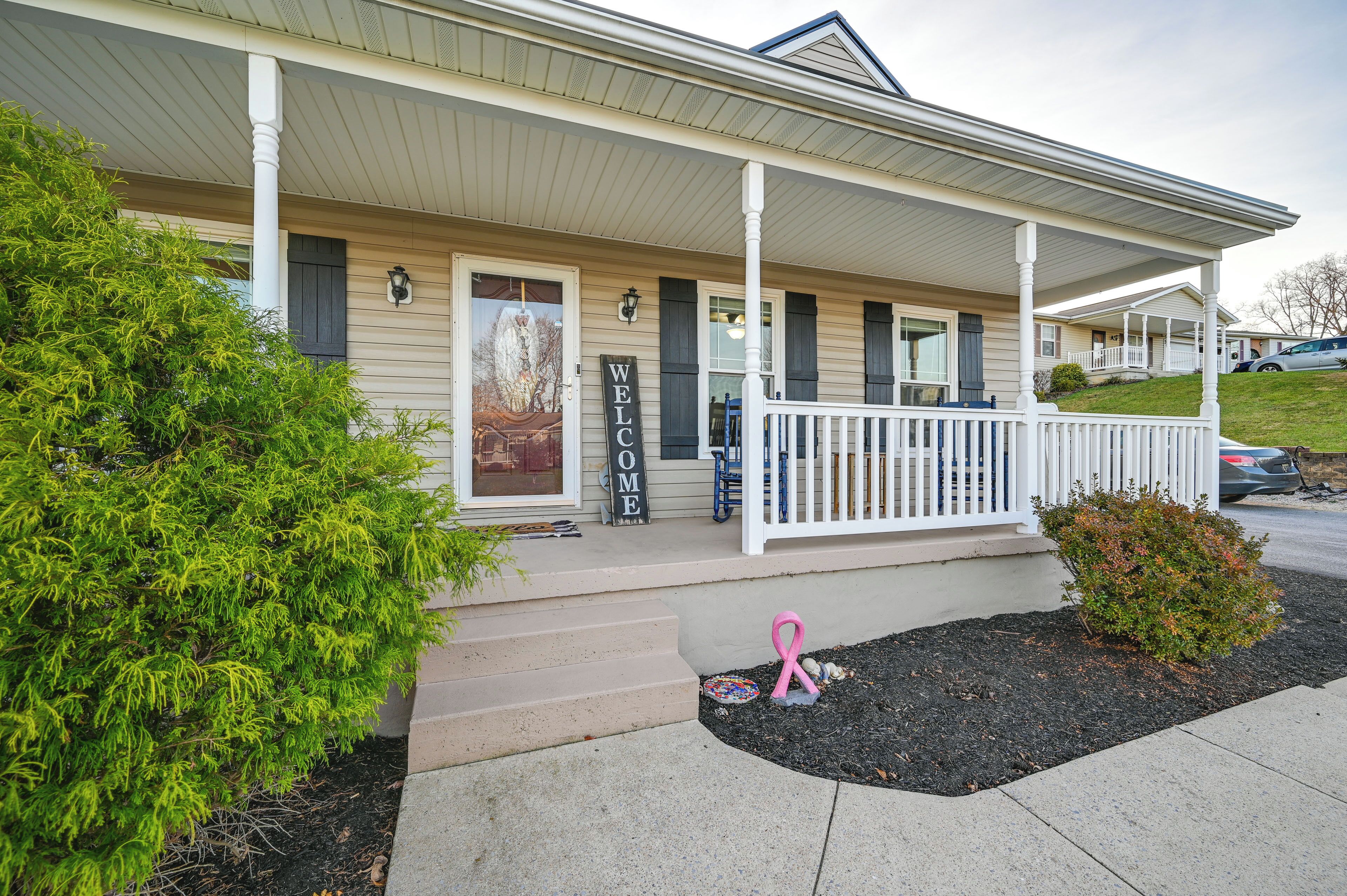 A house with a porch, a welcome sign, and a pink ribbon.