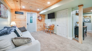 Una habitación acogedora con techo de madera, un sofá, una mesita con sillas y una puerta con un cartel de 'Welcome'.