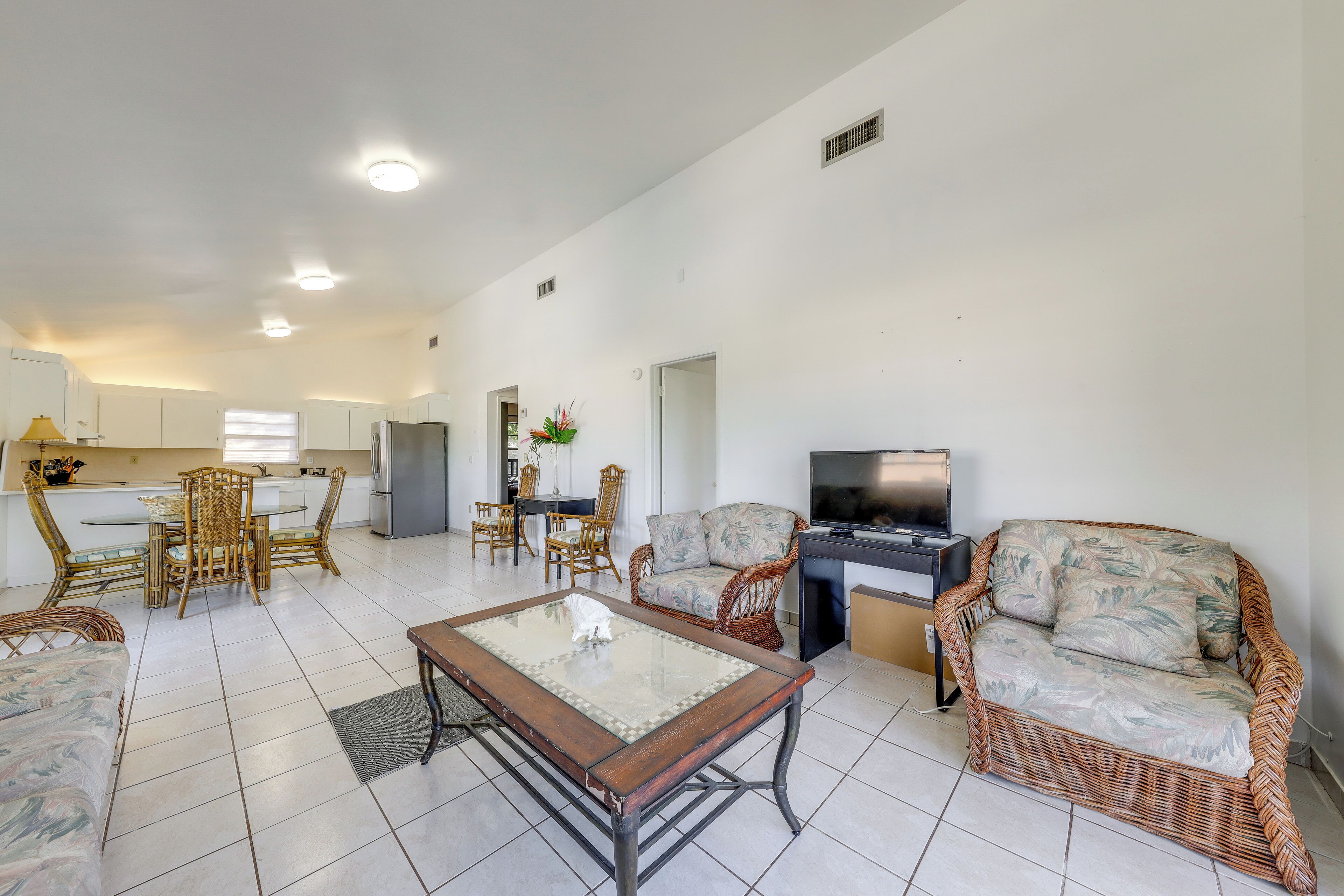 A spacious living area with a dining table, wicker furniture, a sofa, and a television.