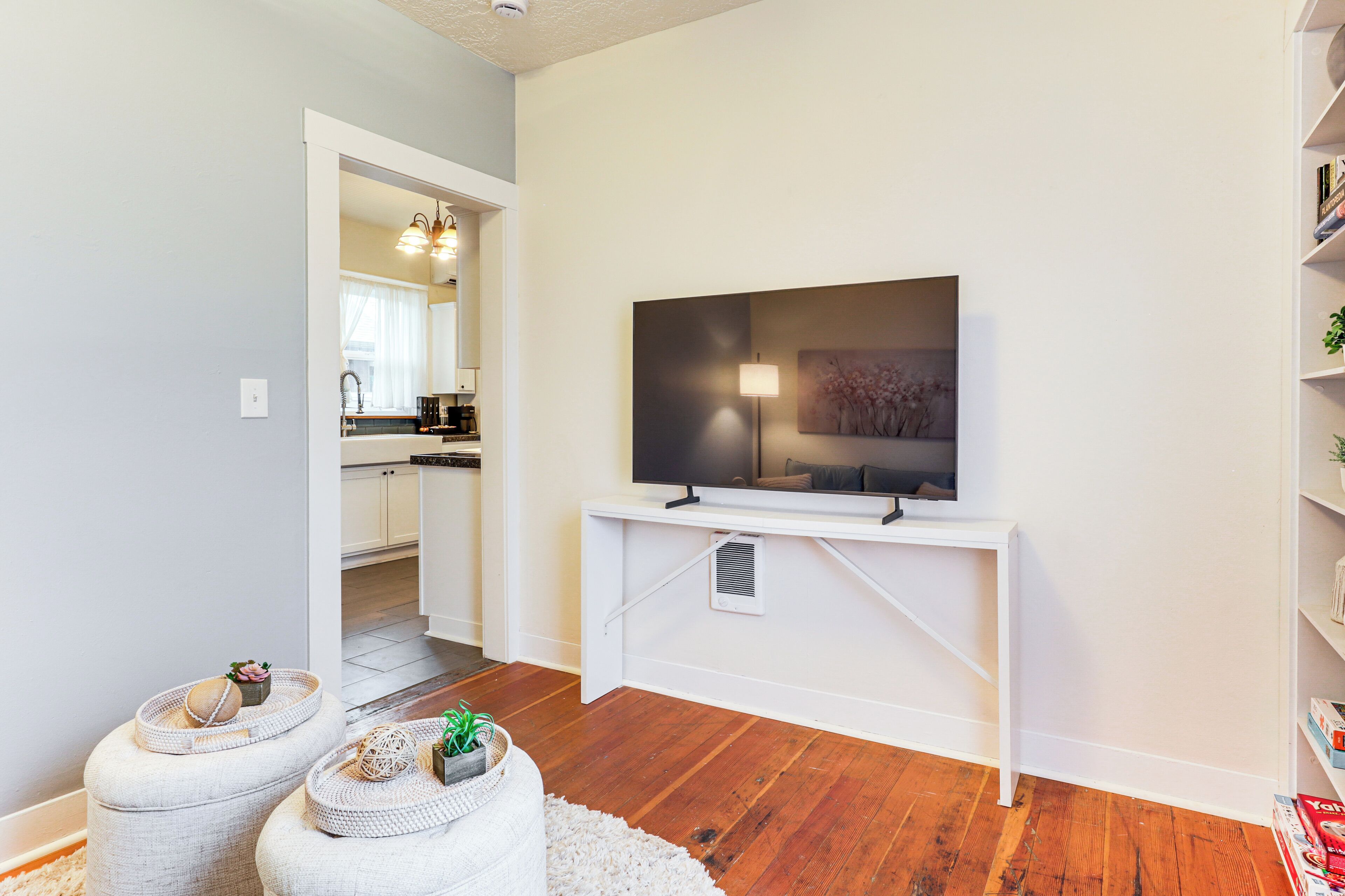 Un salon moderne avec un téléviseur à écran plat posé sur une console blanche, un grand miroir et un canapé blanc agrémenté de coussins décoratifs.