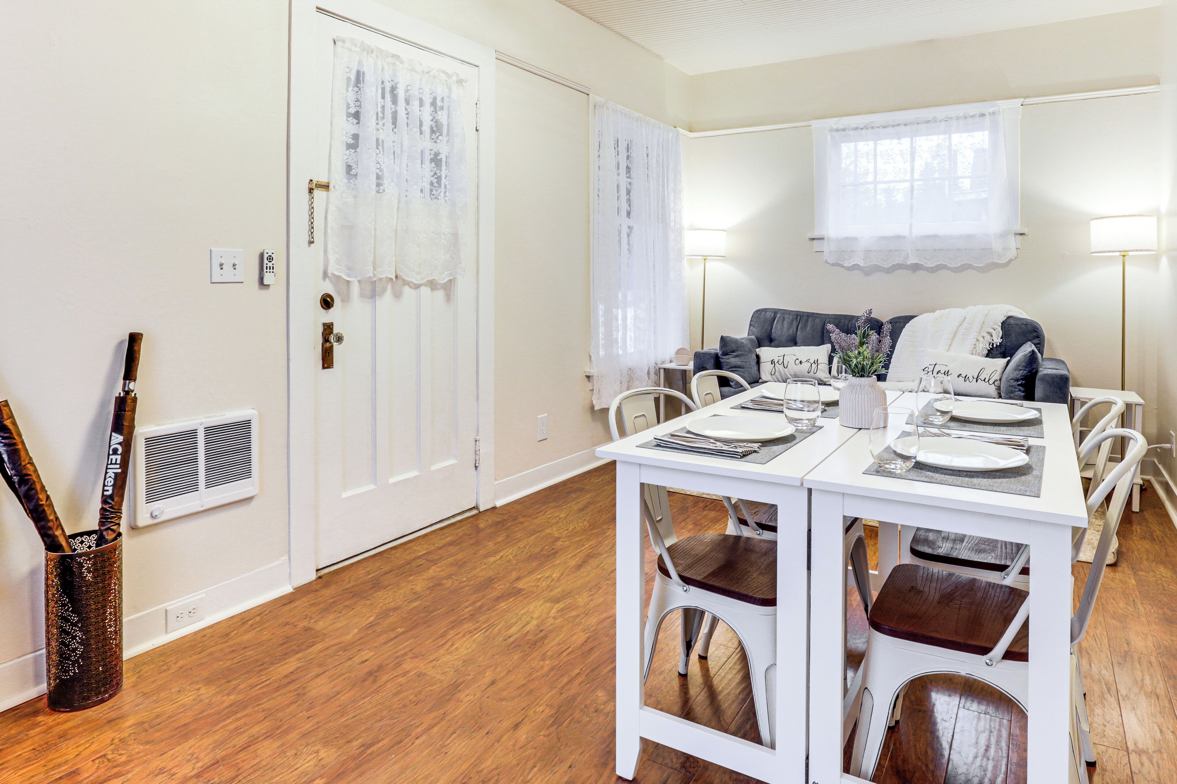 A dining area with a white table set for four, a gray sofa, and a white chair.
