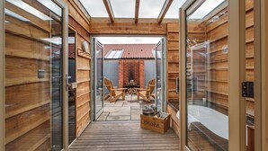 A wooden cabin with a glass door leading to a patio area with a table and chairs. - The Pigs (Melton Constable)