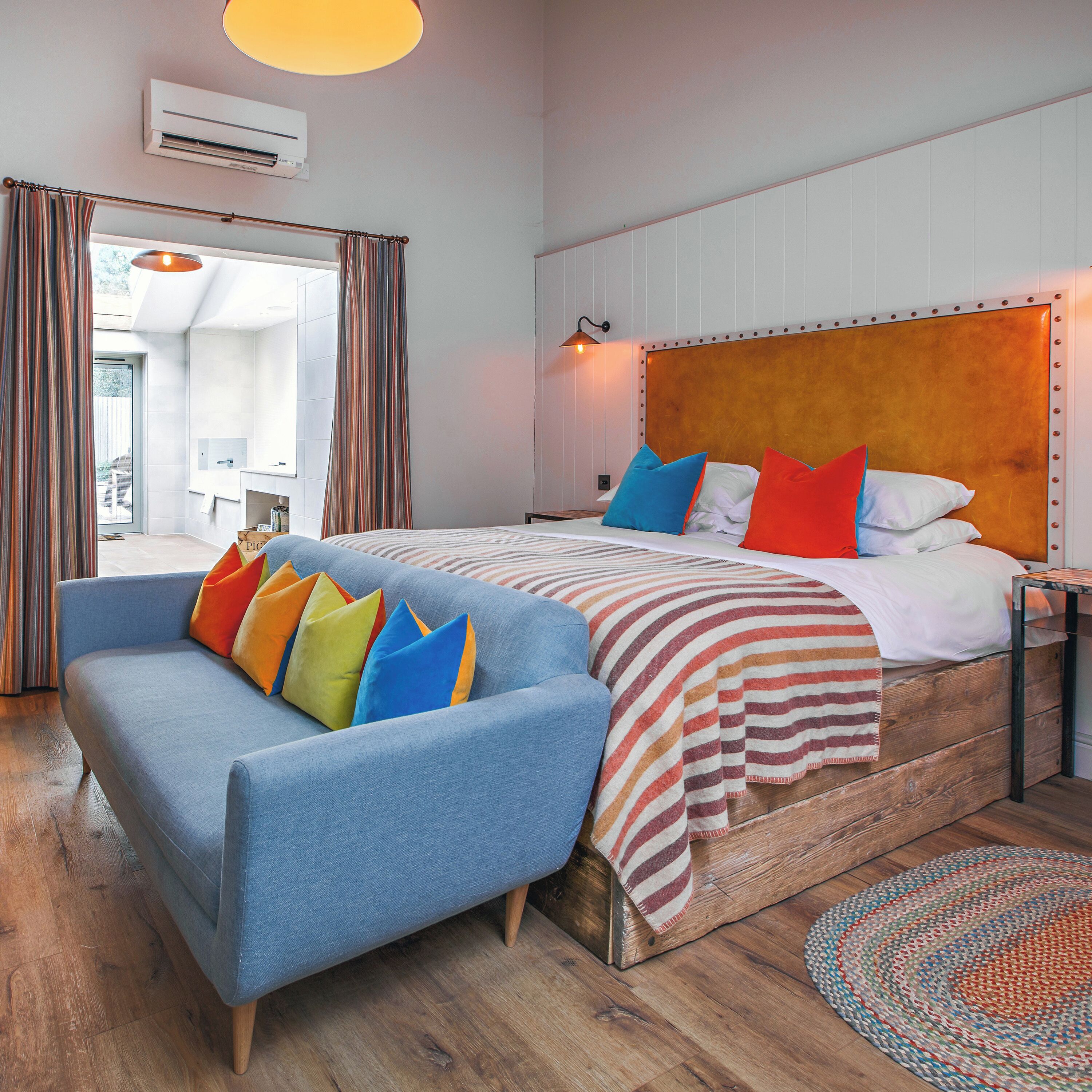 A modern hotel room with a large bed, a blue sofa, and a wooden headboard.