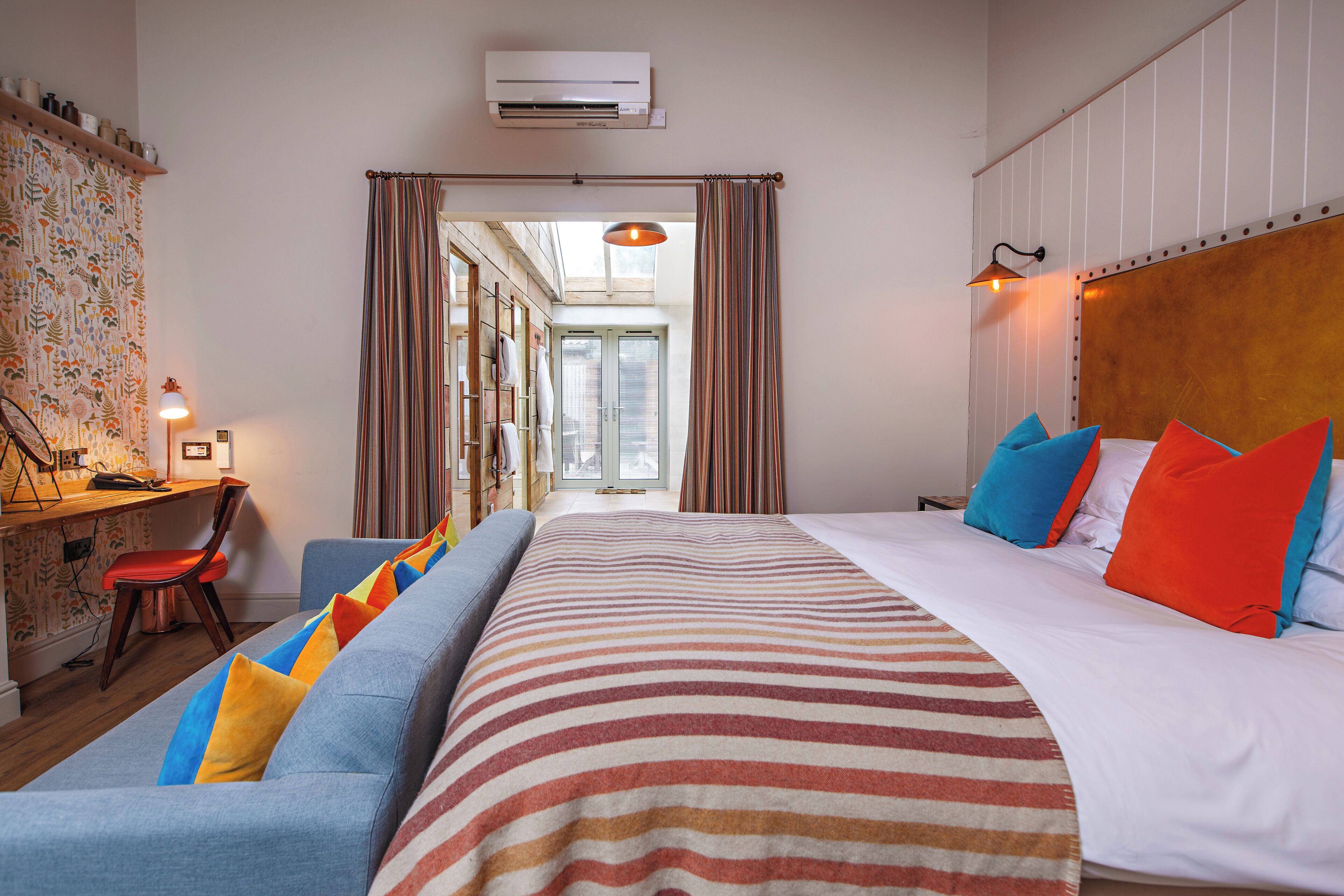 A hotel room with a large bed, a sofa, a desk with a chair, and a view through a door.