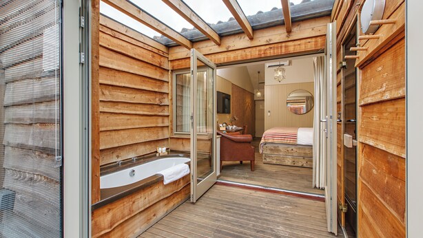 A wooden cabin with a glass door leading to a bathroom with a bathtub and a shower. - The Pigs (Melton Constable)