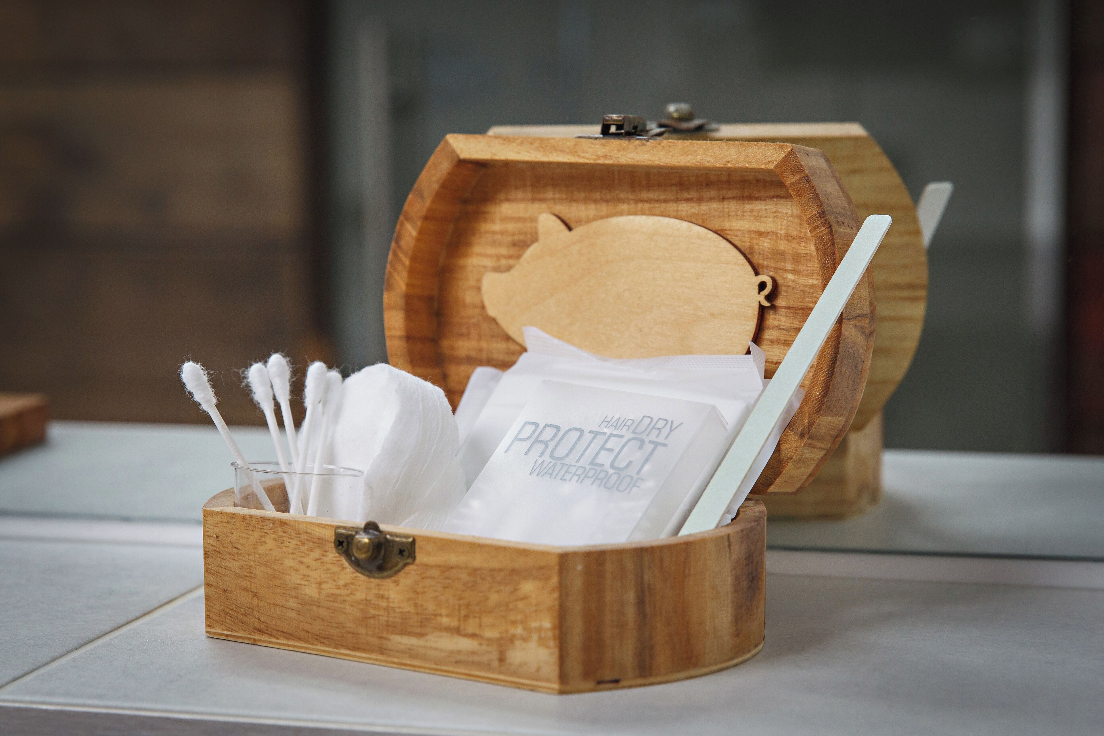 A wooden box with a lock, containing a toothbrush, a white cloth, and a bag labeled "HAIR DRY PROTECT WATERPROOF."