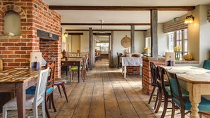 A rustic dining area with brick walls, wooden floors, and a mix of wooden and upholstered chairs. - The Pigs (Melton Constable)