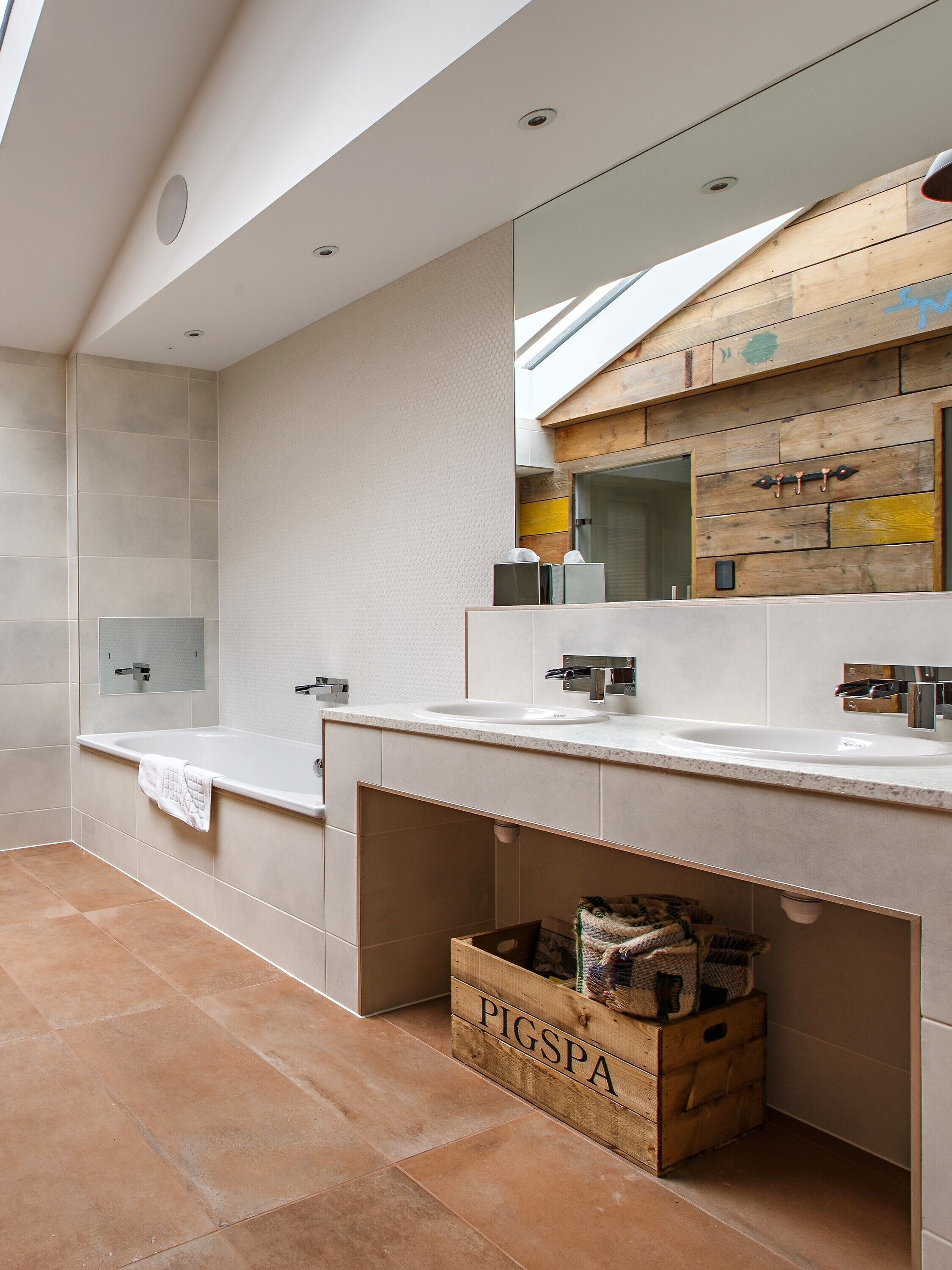 A modern bathroom with two sinks, a large mirror, and a wooden crate labeled "PIGSPA" under the counter.