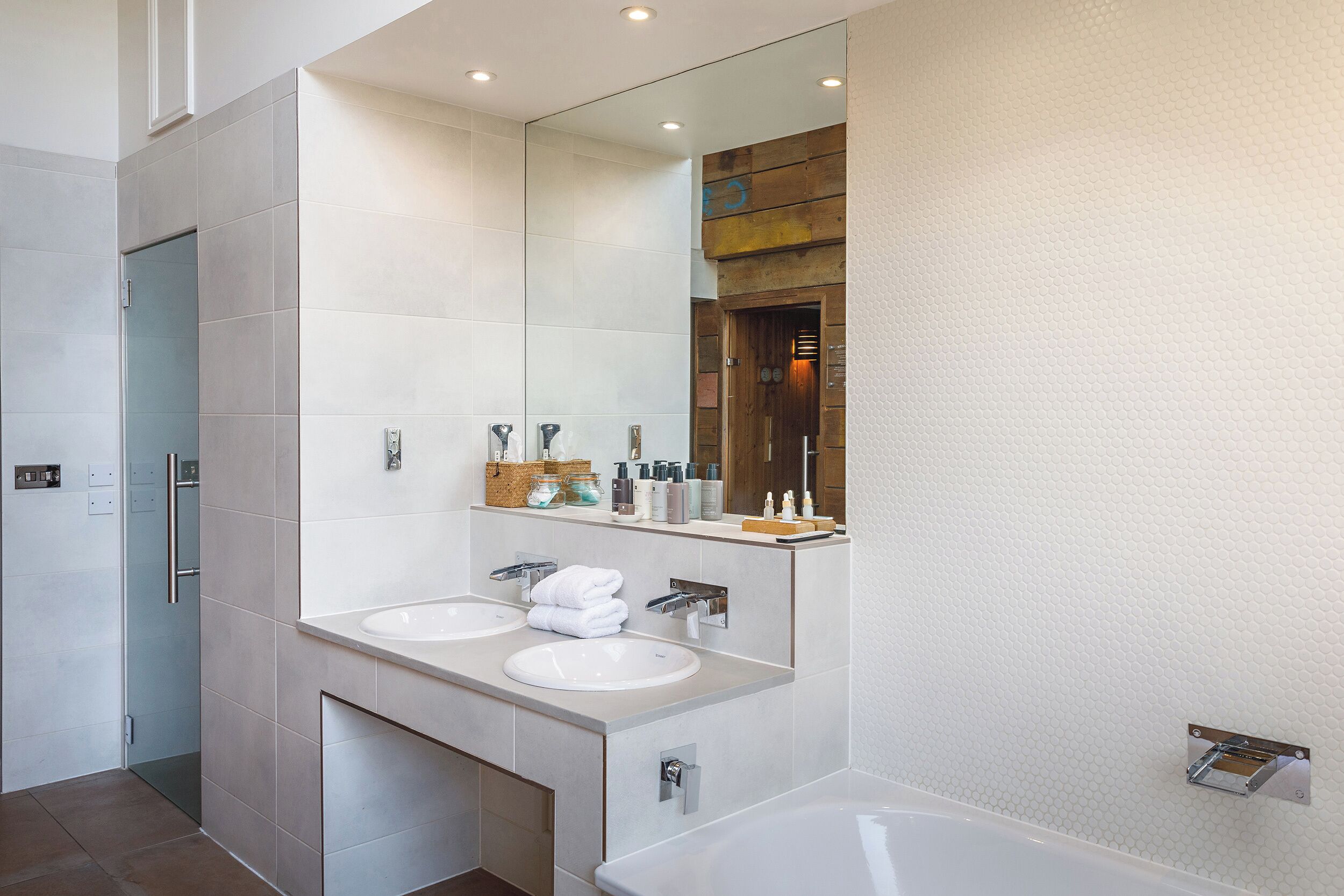 A modern bathroom with two sinks, a large mirror, and a bathtub.