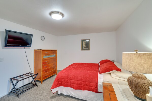 Un dormitorio con cama, televisor, cómoda, reloj y un cuadro en la pared.