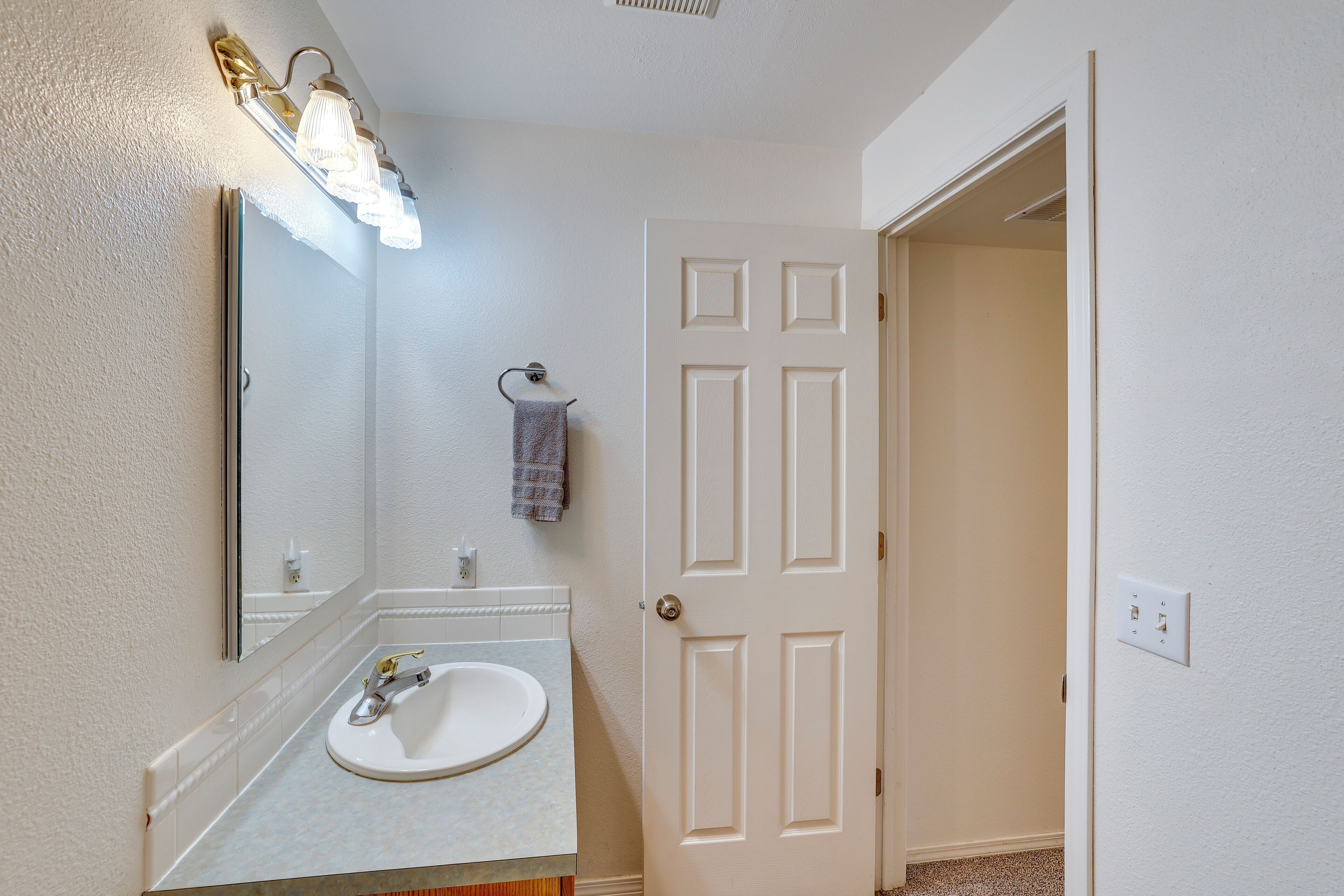 A bathroom with a white sink, mirror, and light fixture.