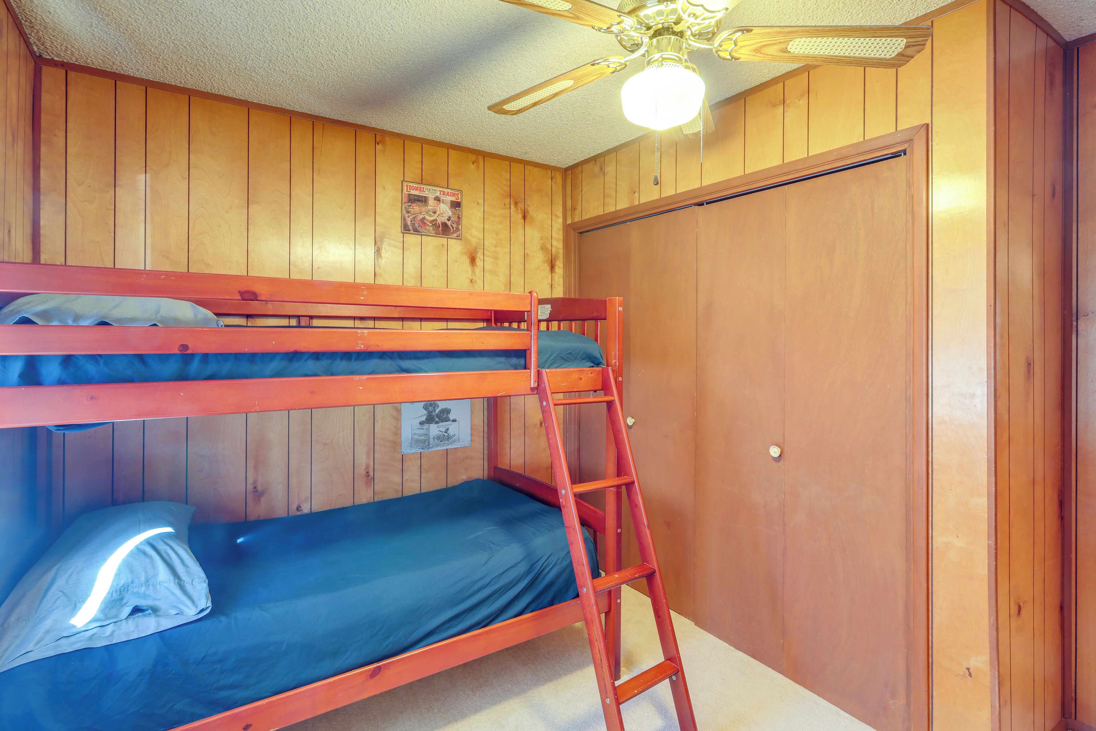 A bunk bed room with wooden walls, a ceiling fan, and a door.