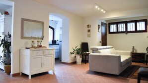 Un vaste salon avec un canapé blanc, un coin repas avec un meuble blanc et une plante en pot, et une cuisine à l’arrière-plan.