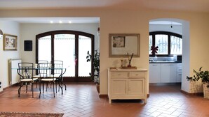 Un vaste espace de vie comprenant une table à manger et des chaises, un meuble blanc et une vue sur la cuisine par le biais d’une arche.