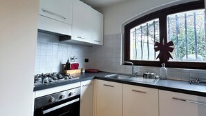 Une cuisine moderne avec des meubles blancs, une cuisinière à gaz et une fenêtre donnant sur un paysage verdoyant.