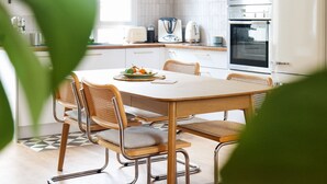 A modern kitchen with white cabinets, stainless steel appliances, and a dining area with a wooden table and wicker chairs. - Superb House in the Gare District - Angers, for 4 People (Angers)