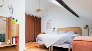 A bedroom with a wooden floor, a bed with a grey blanket, a wooden cabinet with books, and a window with brown curtains. - Superb House in the Gare District - Angers, for 4 People (Angers)