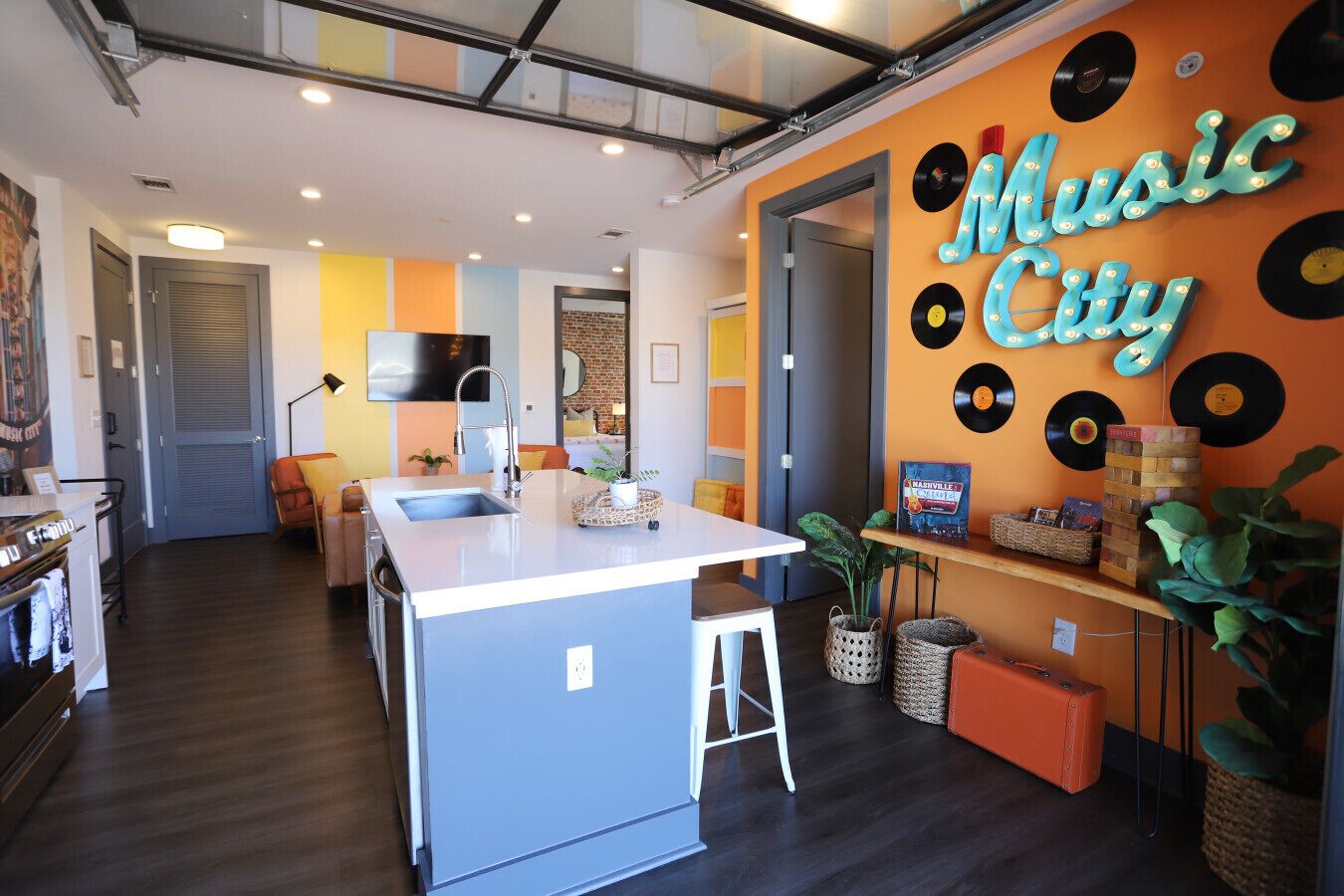 A modern kitchen with a central island, a dining area with a sofa and chairs, and a wall with a 'Music City' sign and vinyl records.
