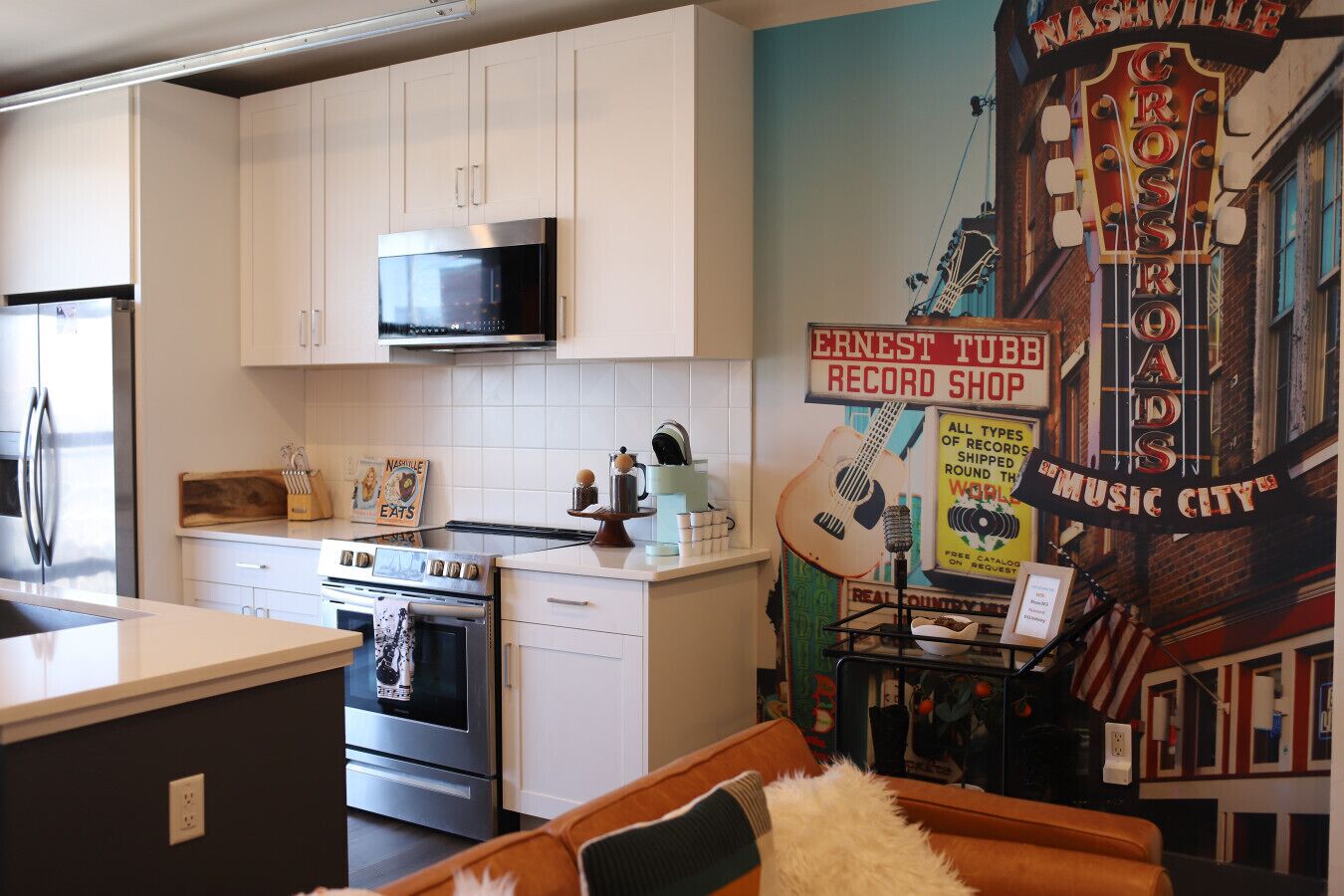 A kitchen with white cabinets, a microwave, an oven, and a coffee maker. There is a mural on the wall depicting a record shop and a guitar.
