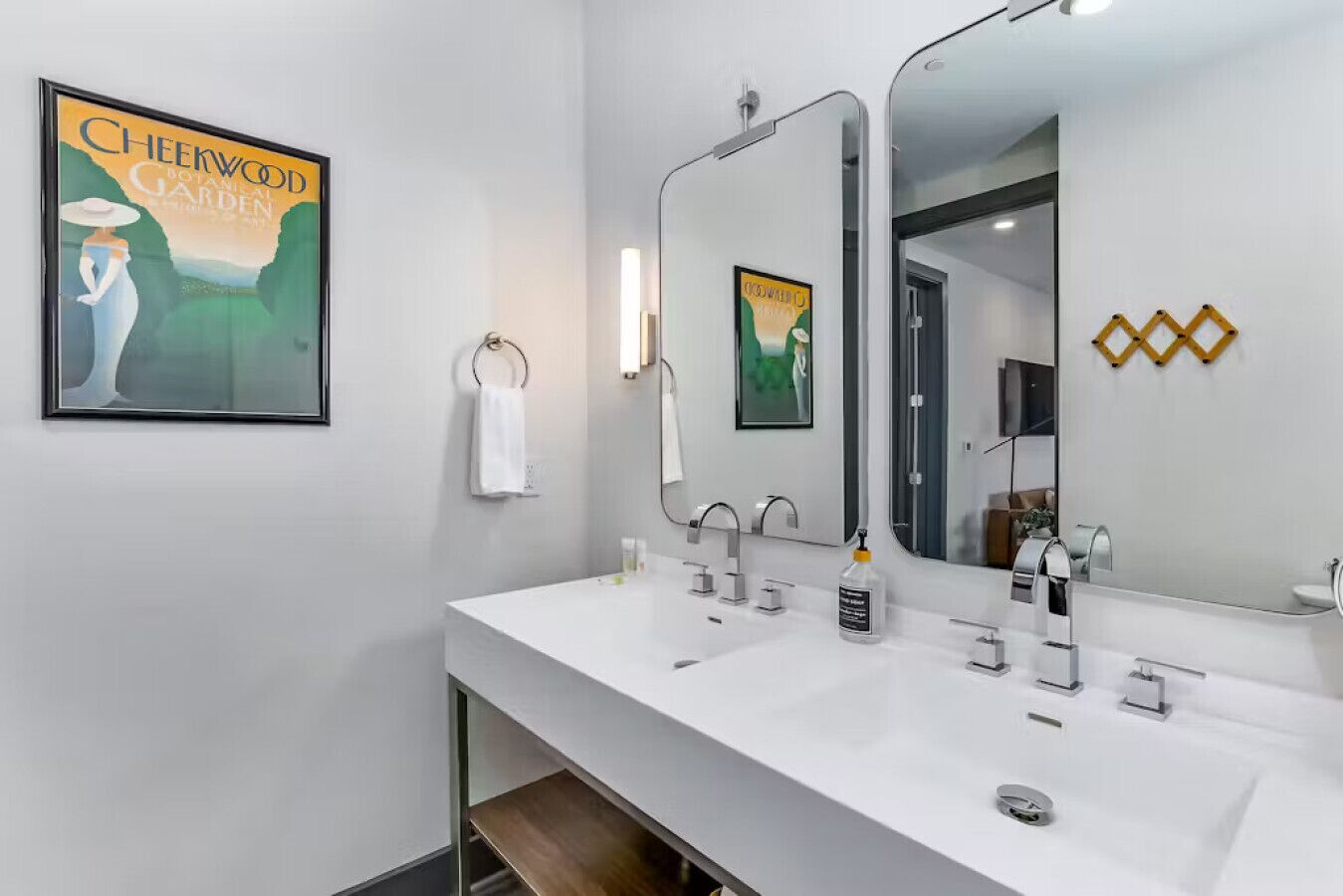 Un baño moderno con dos lavamanos, un espejo grande y un cartel con un jardín.