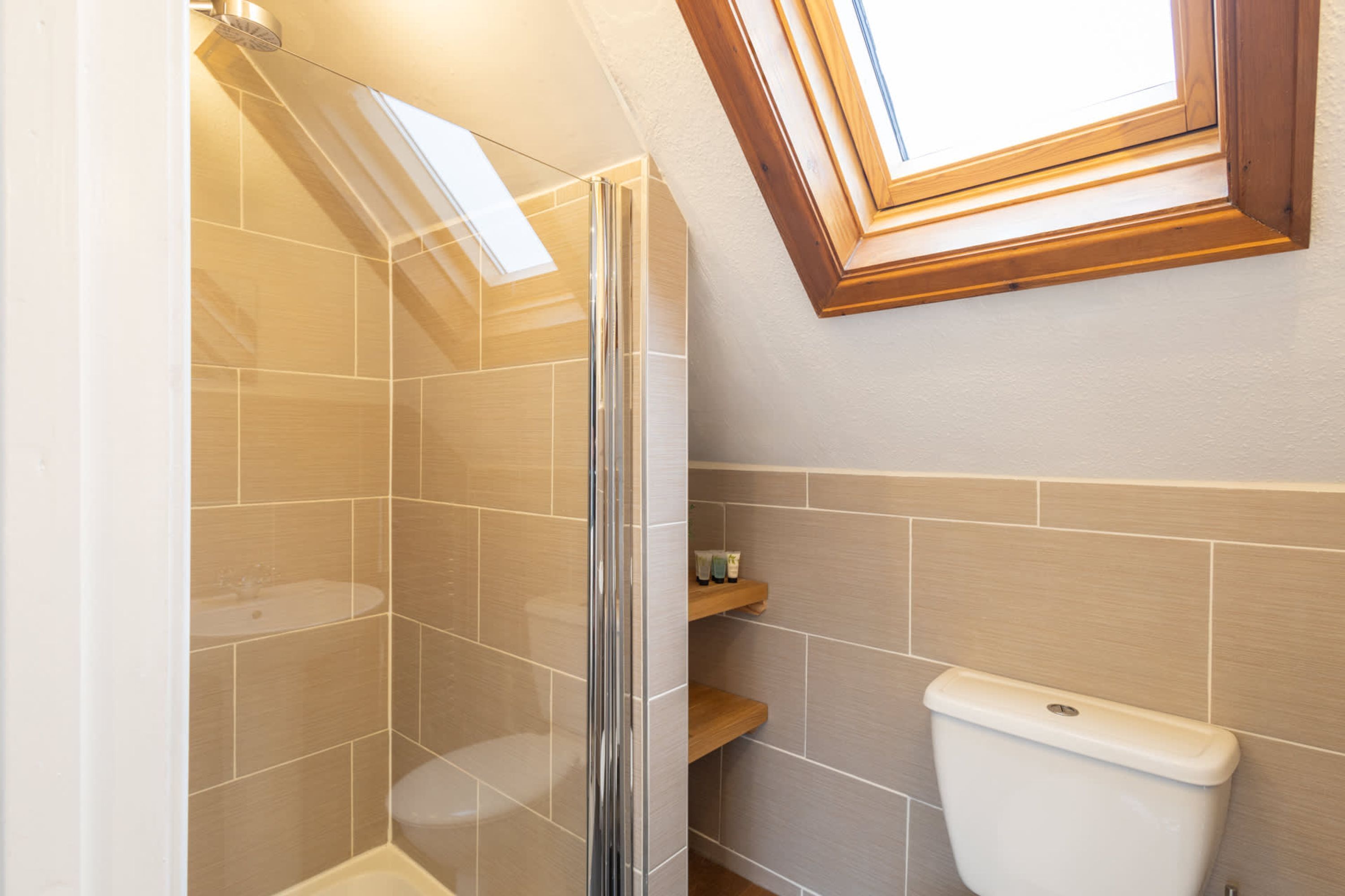 Ein Badezimmer mit Glasdusche, Toilette und Dachfenster über dem Waschbecken.