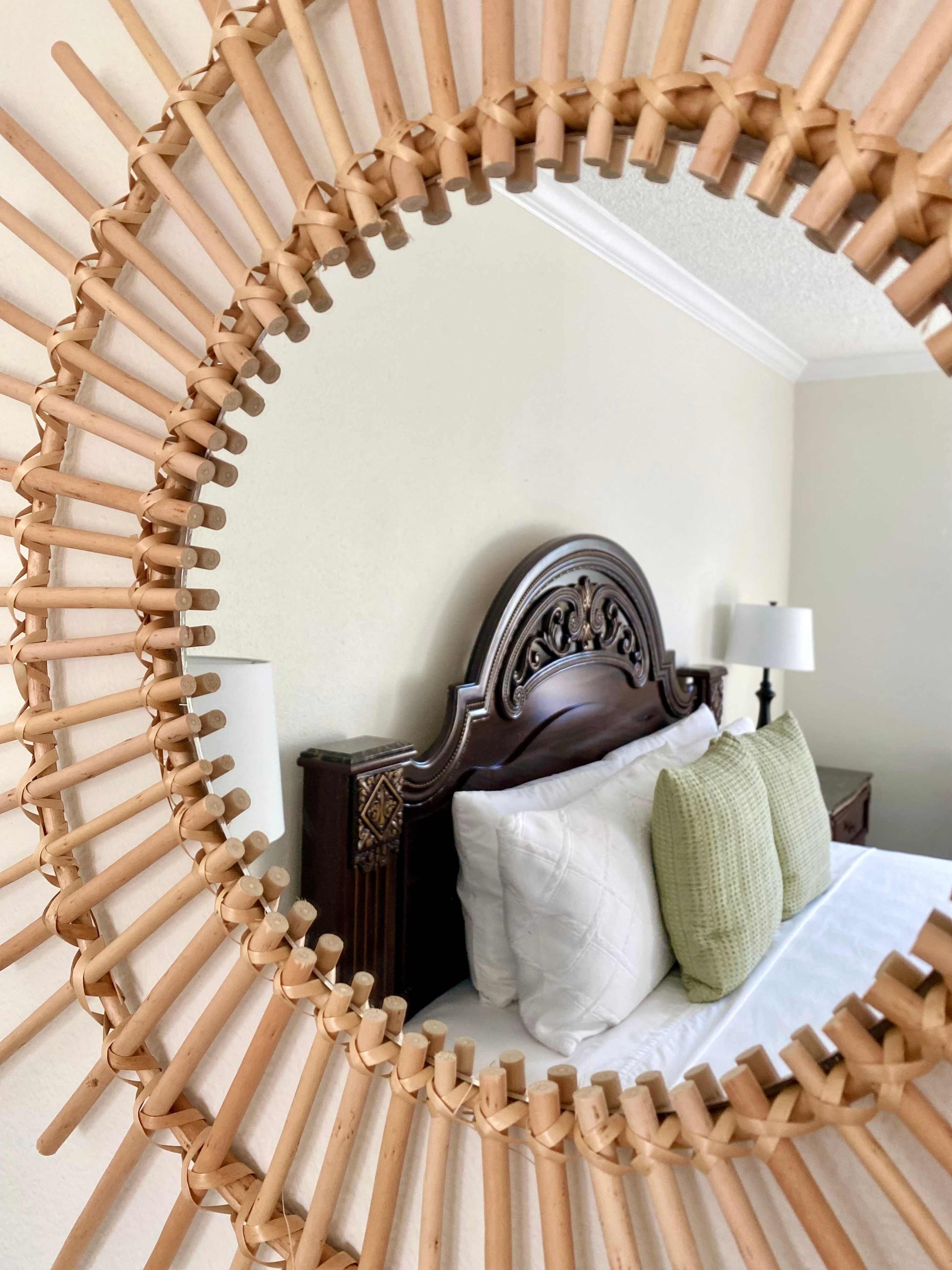 Una habitación con un cabecero de madera, una cama con ropa de cama blanca y una mesita de noche con una lámpara, todo enmarcado por un diseño circular tejido.