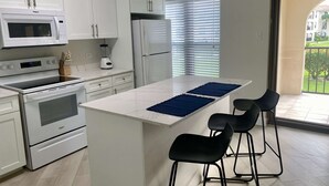 Una cocina moderna con armarios blancos, microondas integrado, refrigerador y una isla central con taburetes de bar.