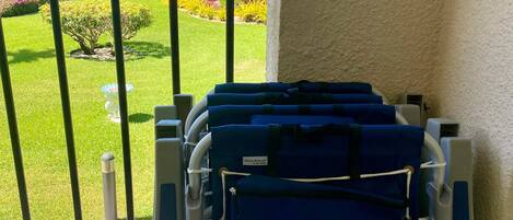 A luggage cart with a 'Rio Beach' pouch on a balcony overlooking a landscaped garden and a building with a tiled roof.