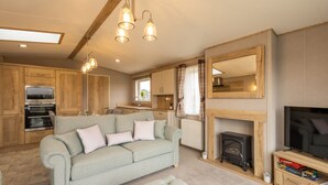Ein gemütliches Wohnzimmer mit Sofa, Kamin, Fernseher und einer Küchenzeile mit Holzschränken und Herd.