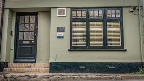 A building with a black door, two windows with shutters, and a sign indicating '34a Coombe Street The Bothy'. - Host Stay The Bothy (Lyme Regis)