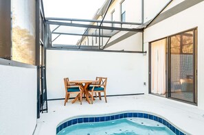 A sunlit patio with a hot tub, a table with chairs, and a glass door leading to a building. - Amazing 5BD Family Townhouse at Paradiso Grande (Orlando)