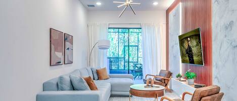 A modern living room with a sofa, armchairs, a coffee table, and a TV on a wall.