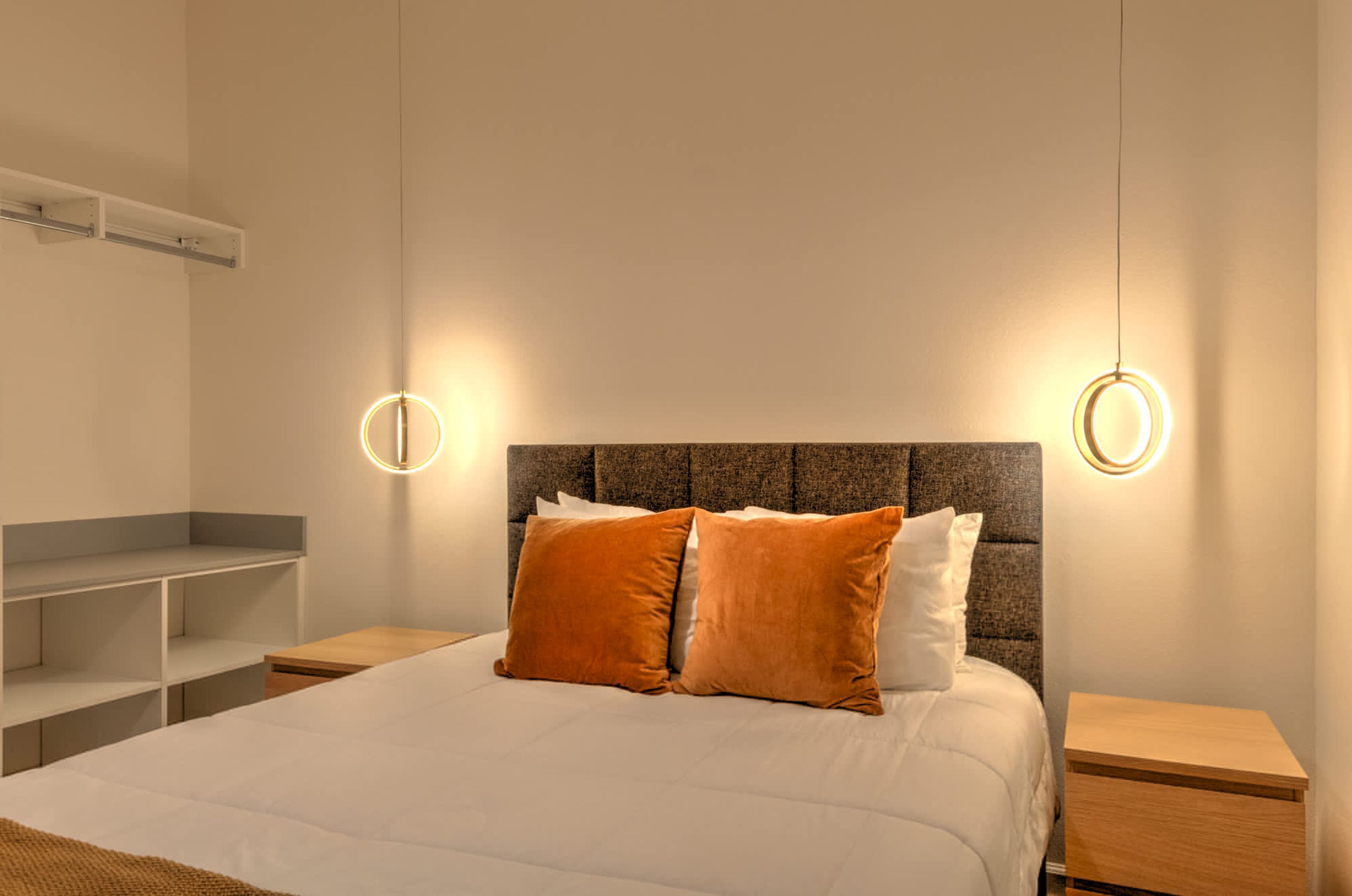 A modern bedroom with a large bed, two nightstands, a built-in shelf, and circular wall sconces.