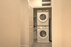 A compact laundry room with a front-loading washer and dryer, a door, and a wall-mounted sign above the dryer.