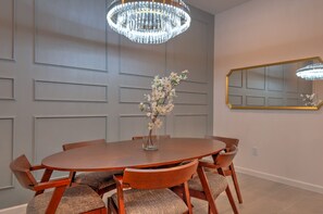 A dining room with a round wooden table, six chairs, a vase with flowers, a chandelier, and a mirror on the wall. - Amazing 5BD Family Townhouse at Paradiso Grande (Orlando)