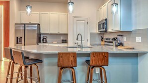A modern kitchen with white cabinets, stainless steel appliances, a large island with bar stools, and pendant lighting. - Amazing 5BD Family Townhouse at Paradiso Grande (Orlando)