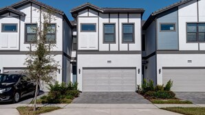 A row of modern townhouses with white exteriors, grey trim, and a central garage. - Amazing 5BD Family Townhouse at Paradiso Grande (Orlando)