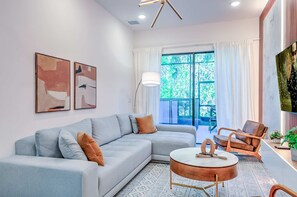 A modern living room with a light blue sofa, a round coffee table, and a large window with curtains. - Amazing 5BD Family Townhouse at Paradiso Grande (Orlando)