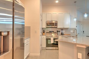 A modern kitchen with stainless steel appliances, white cabinetry, and a granite countertop. - Amazing 5BD Family Townhouse at Paradiso Grande (Orlando)