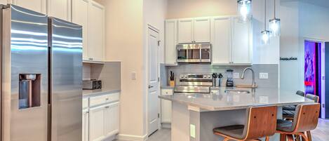 A modern kitchen with stainless steel appliances, white cabinetry, and a central island with bar stools.