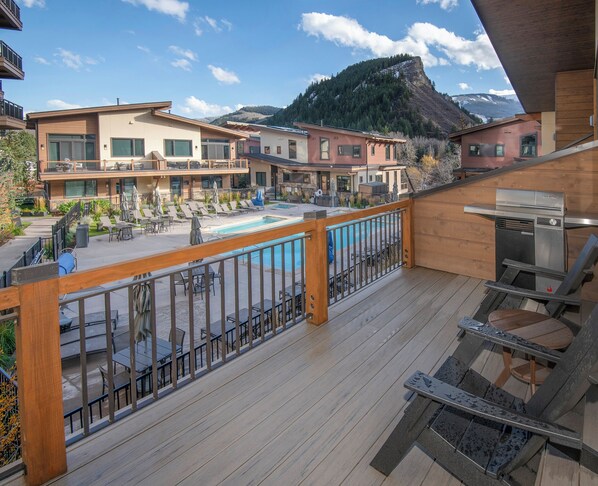 A wooden deck with a pool, lounge chairs, and a grill area.