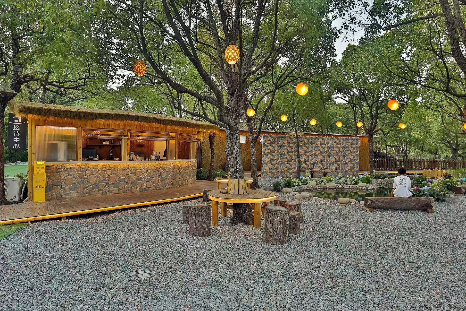 Un área de estar al aire libre rústica con paredes de piedra, mesas de madera y luces colgantes.