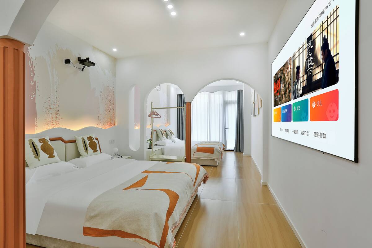A modern hotel room with a large bed, a desk, and a wall-mounted TV displaying a movie.